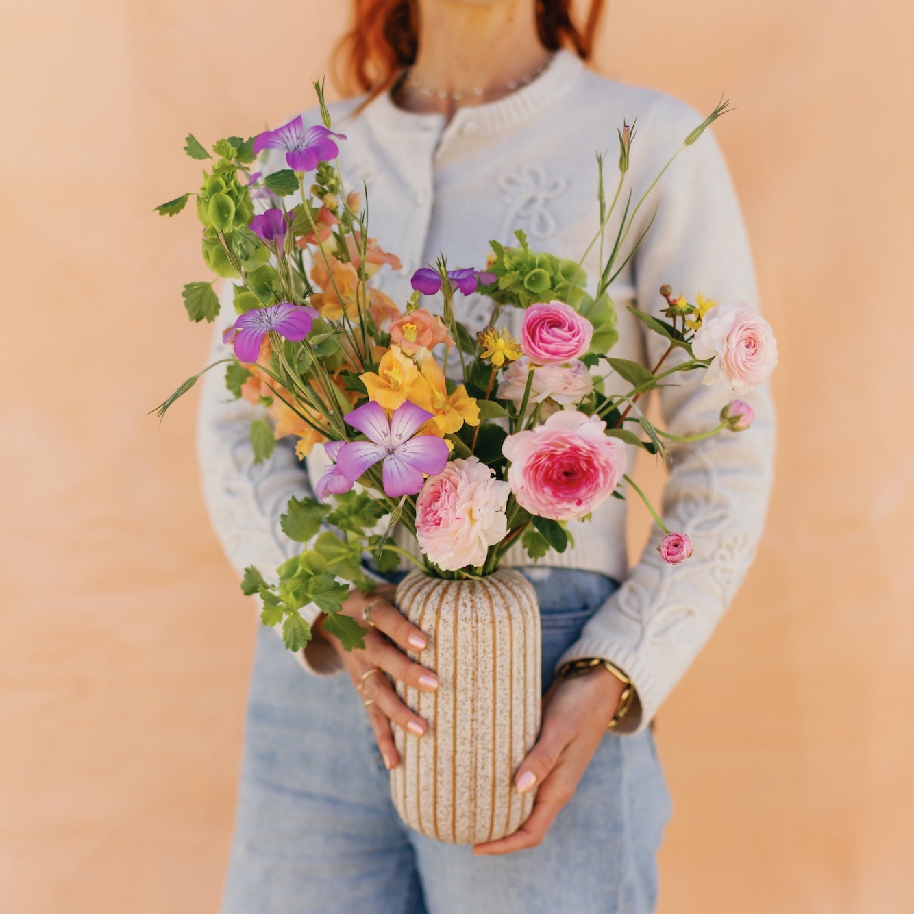 Person holding a vase with colorful flowers against a beige background