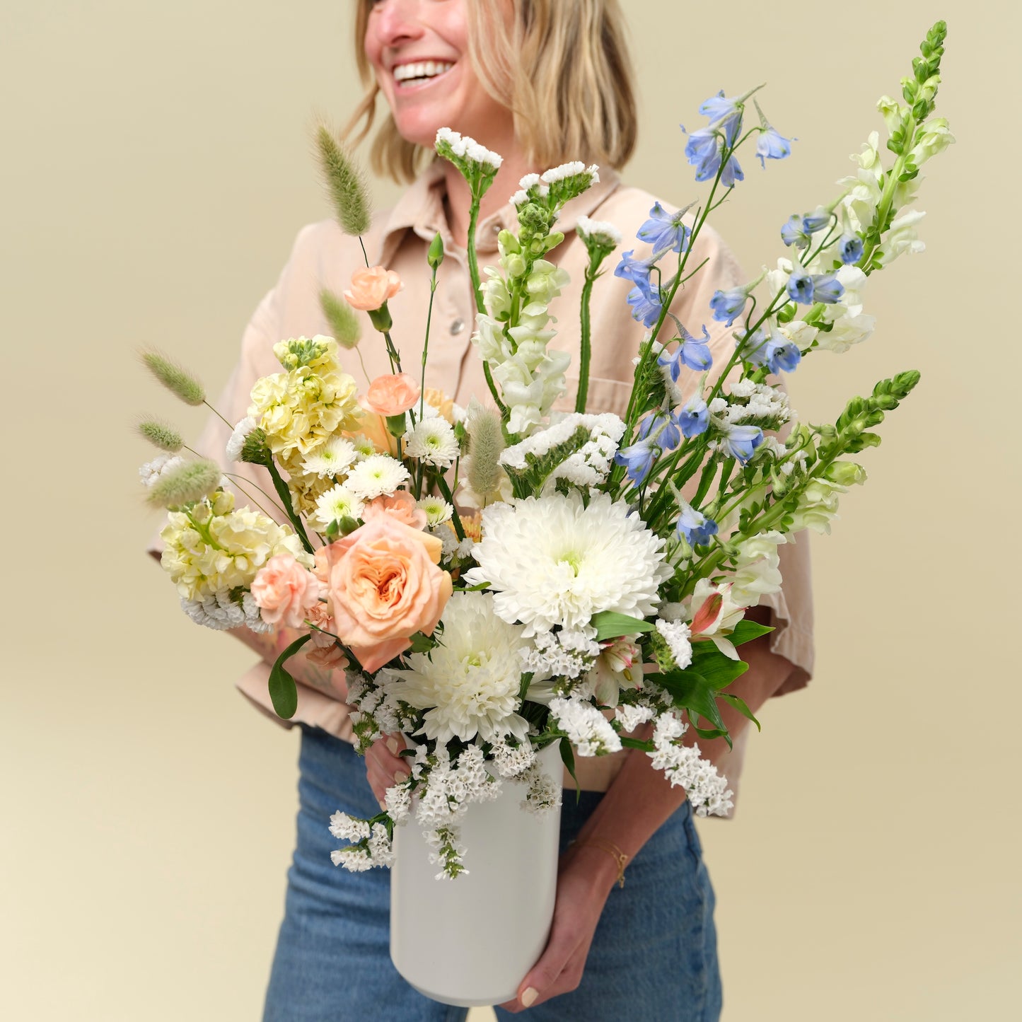 Natalie holding a tall vase of flowers in shades of white, peach, yellow, and blue