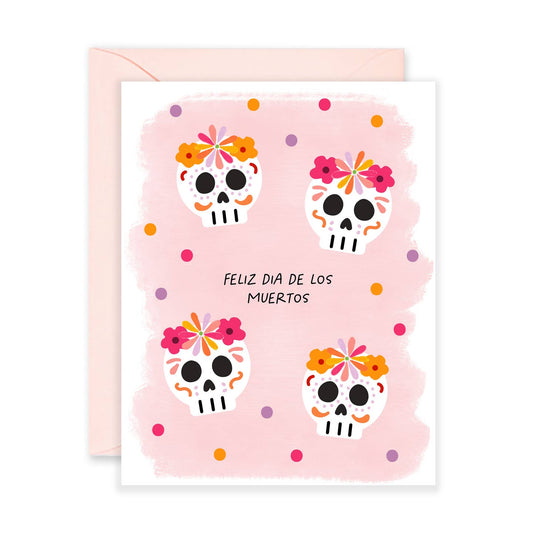 Greeting card with colorful skull designs and 'Feliz Dia de los Muertos' text on a pink background.