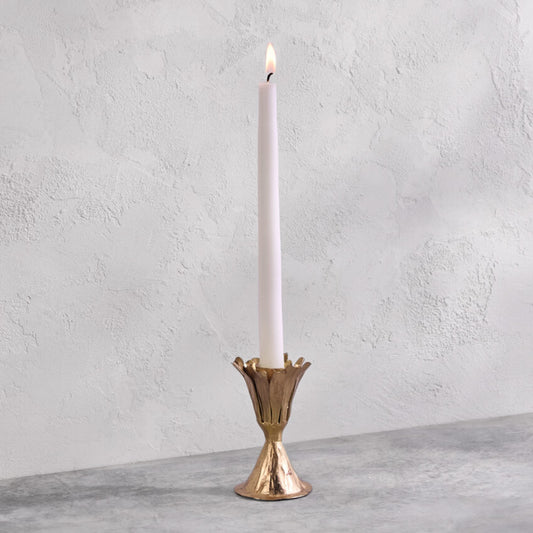Gold candle holder with a lit white candle on a gray surface and light gray background