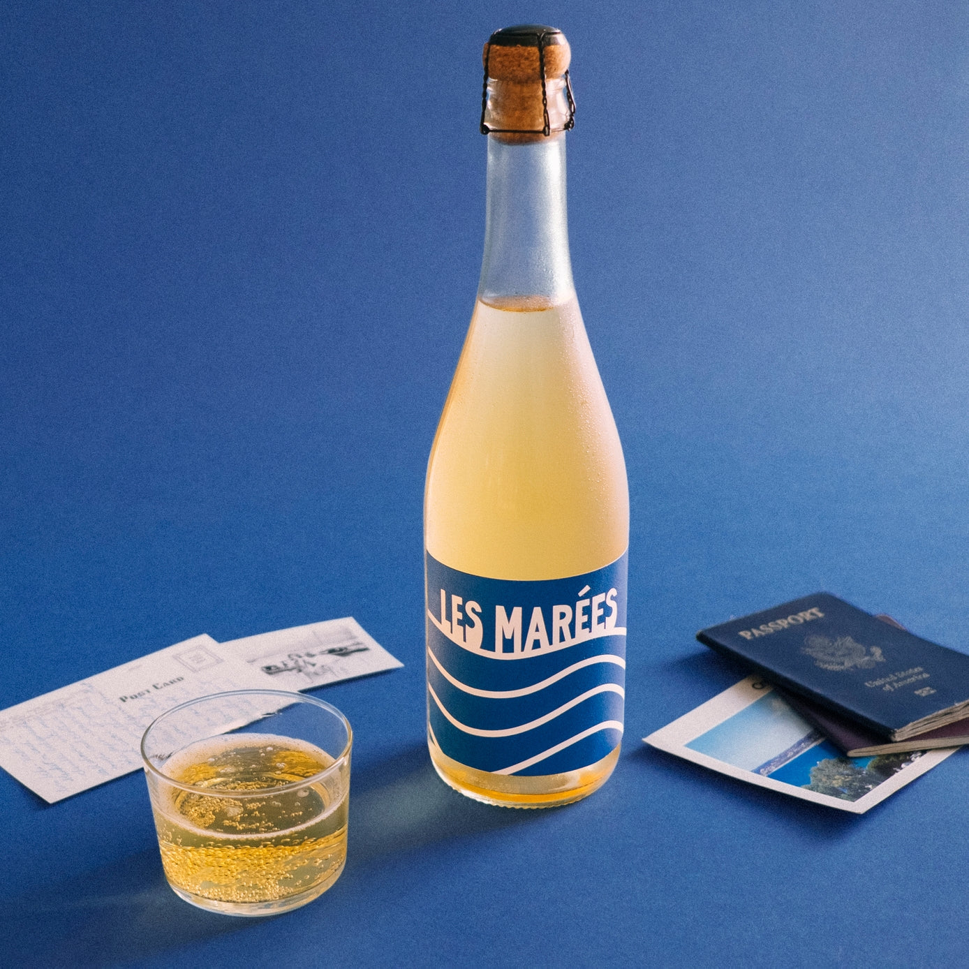 Bottle of 'Les Marées' sparkling wine with a glass on a blue background