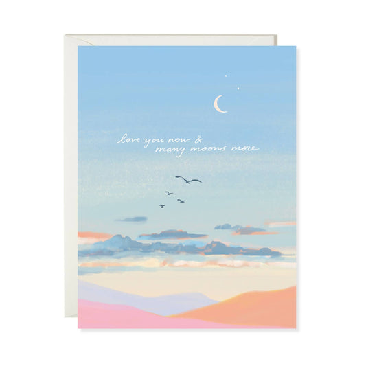 Greeting card with a desert landscape and text 'Love you now & many moons more' on a blue sky background.