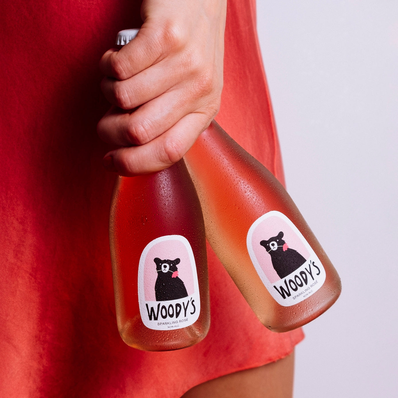 Person holding two bottles of Woody's juice with a red shirt.