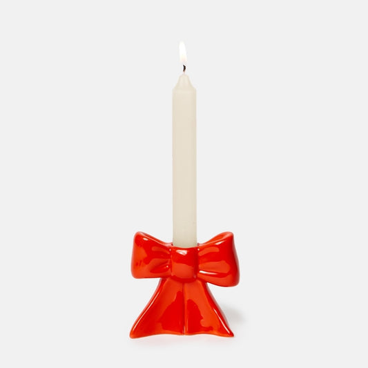 Red bow-shaped candle holder with a white candle on a light gray background