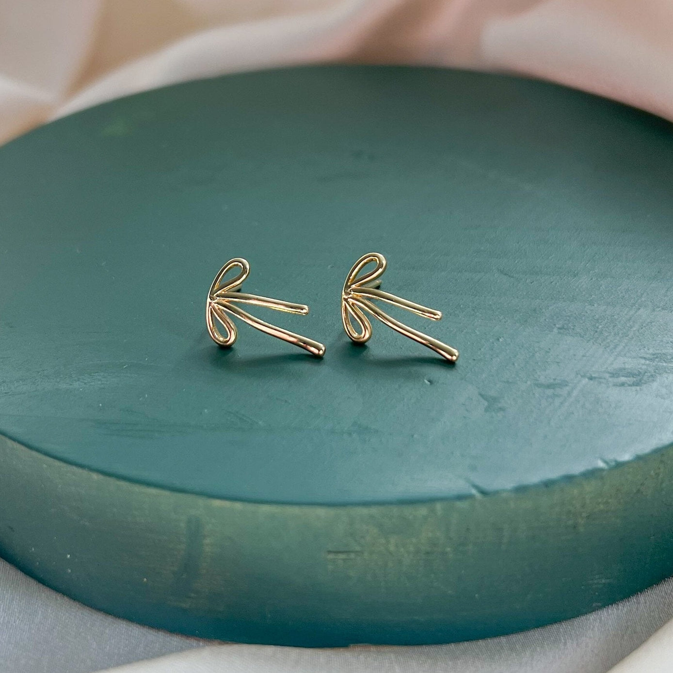 Golden Bow Stud Earringss on a green display
