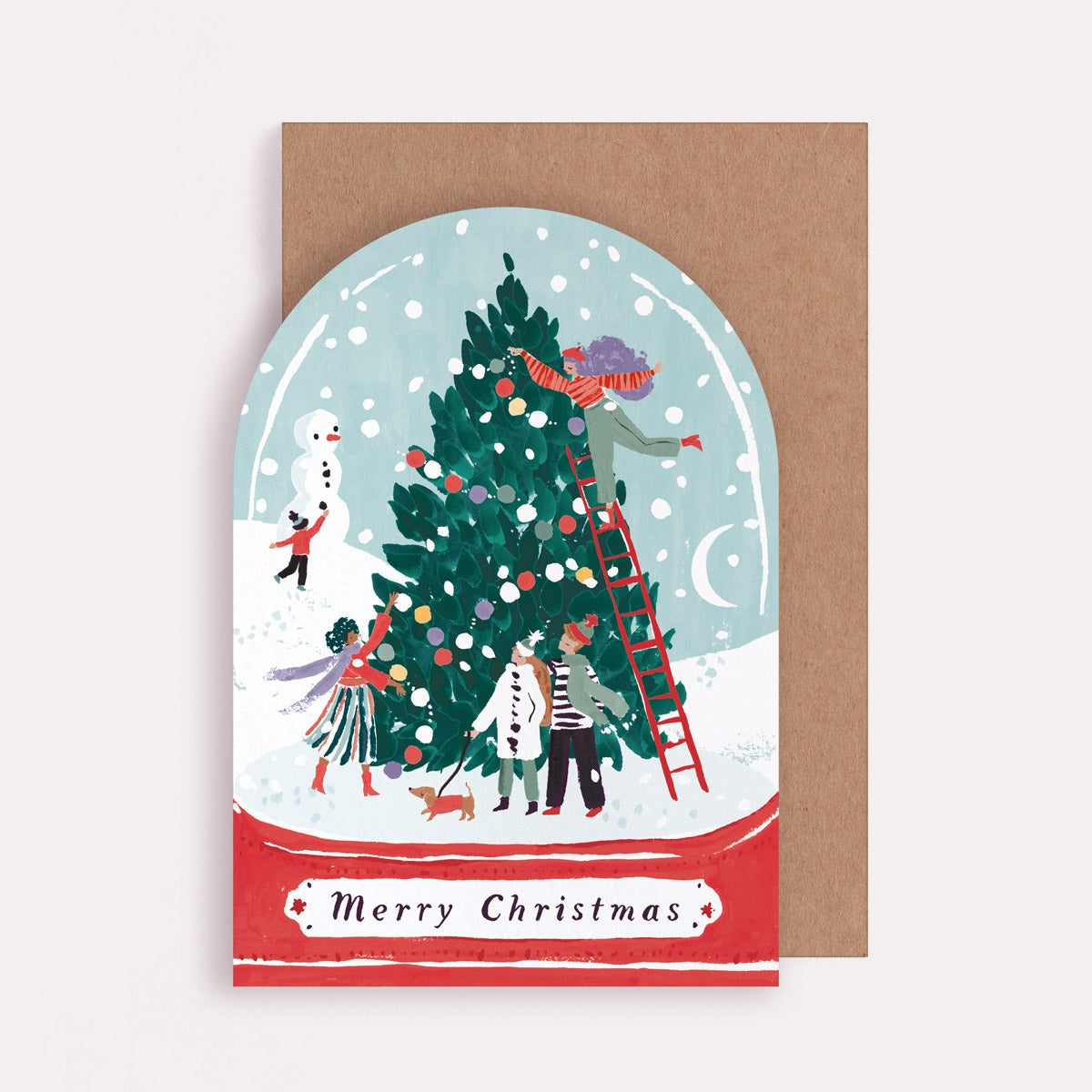 Christmas card with a snowy scene of people decorating a tree, on a brown envelope.