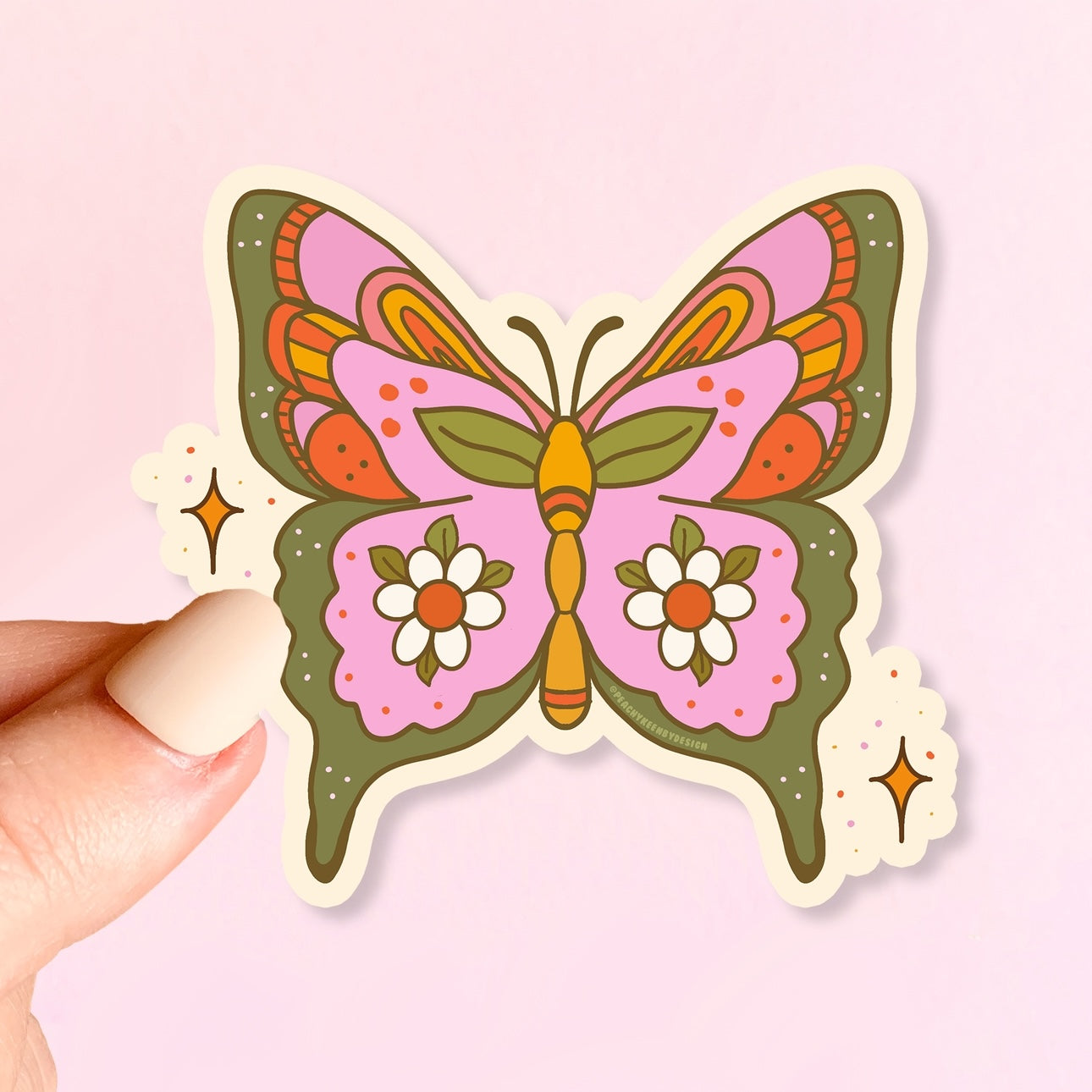 Colorful butterfly-shaped sticker held by a hand against a pink background