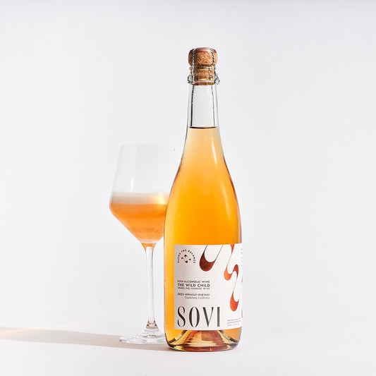 Bottle of SOVI non-alcoholic wine with a glass filled with the same wine on a white background