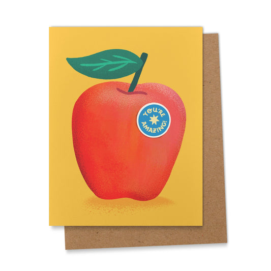Greeting card with a red apple illustration and 'You're Amazing' sticker on a yellow background