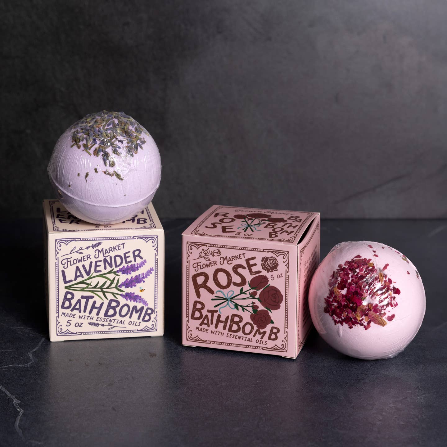 Two bath bombs with their respective boxes on a dark surface