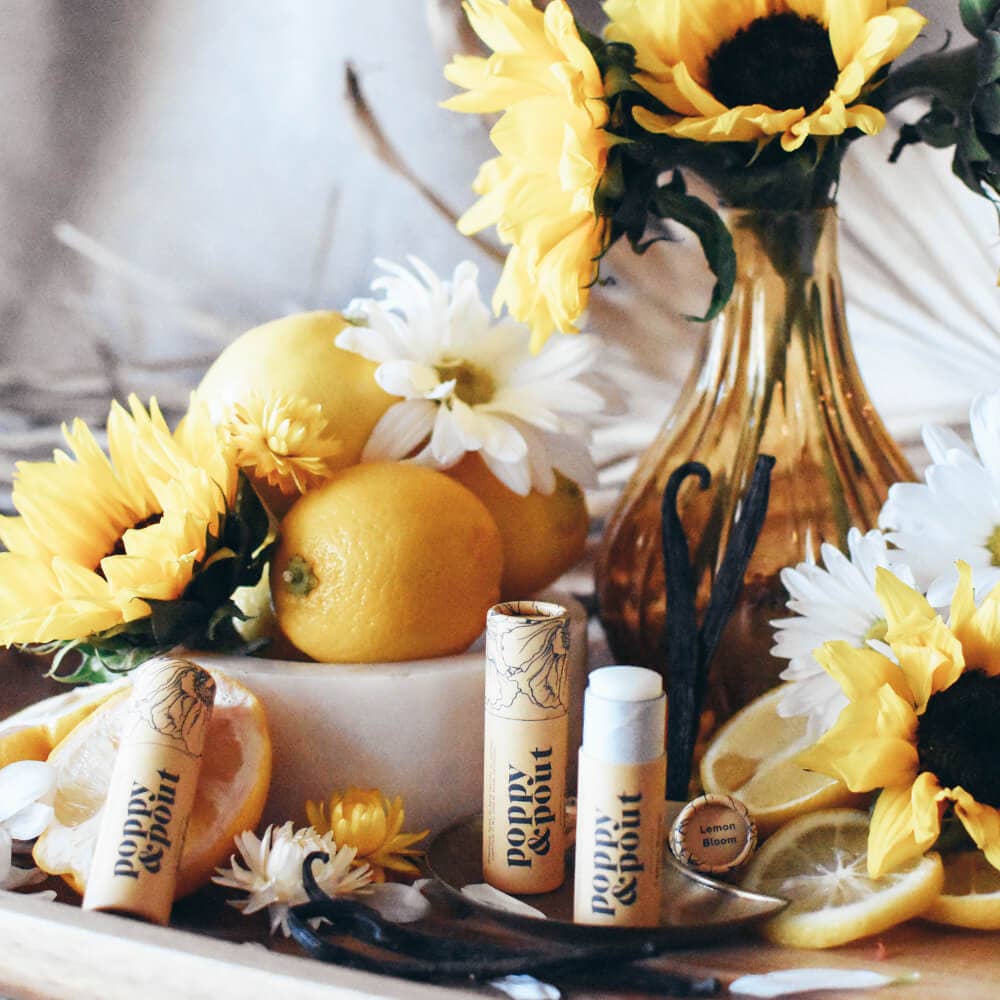 Lemon bloom lip balm tubes displayed next to lemons and sunflowers