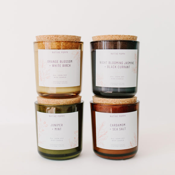 Four scented candles from Native Poppy in colorful glass jars with cork tops