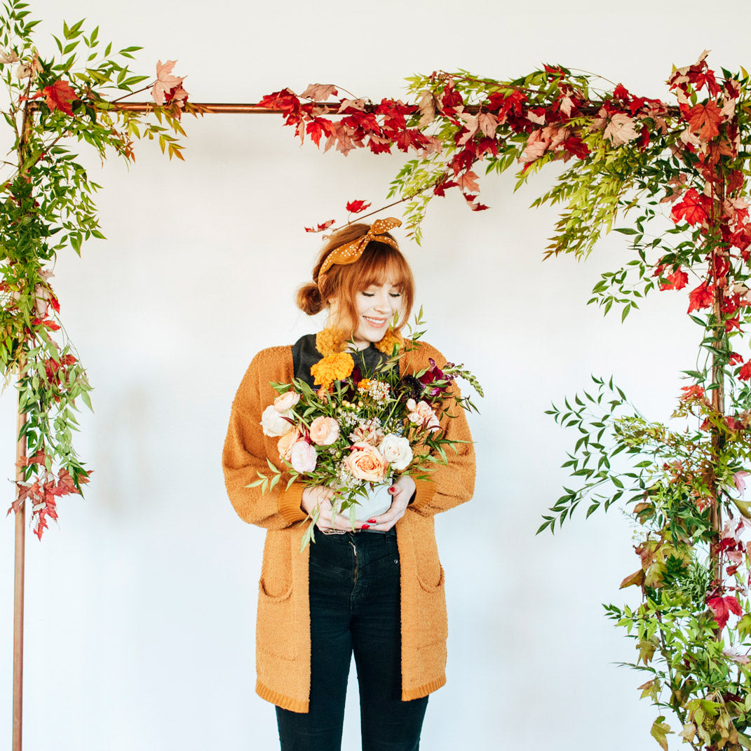 Woman posing under floral decorated archway with her flower arrangement