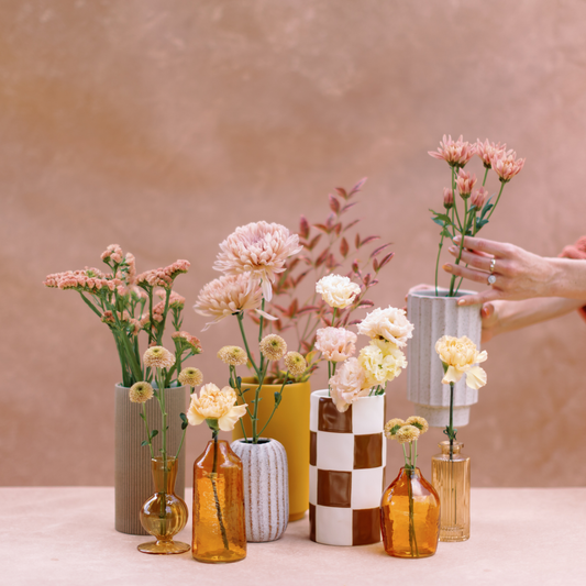 A set of nine fall vases with flowers set up against a peach backdrop.