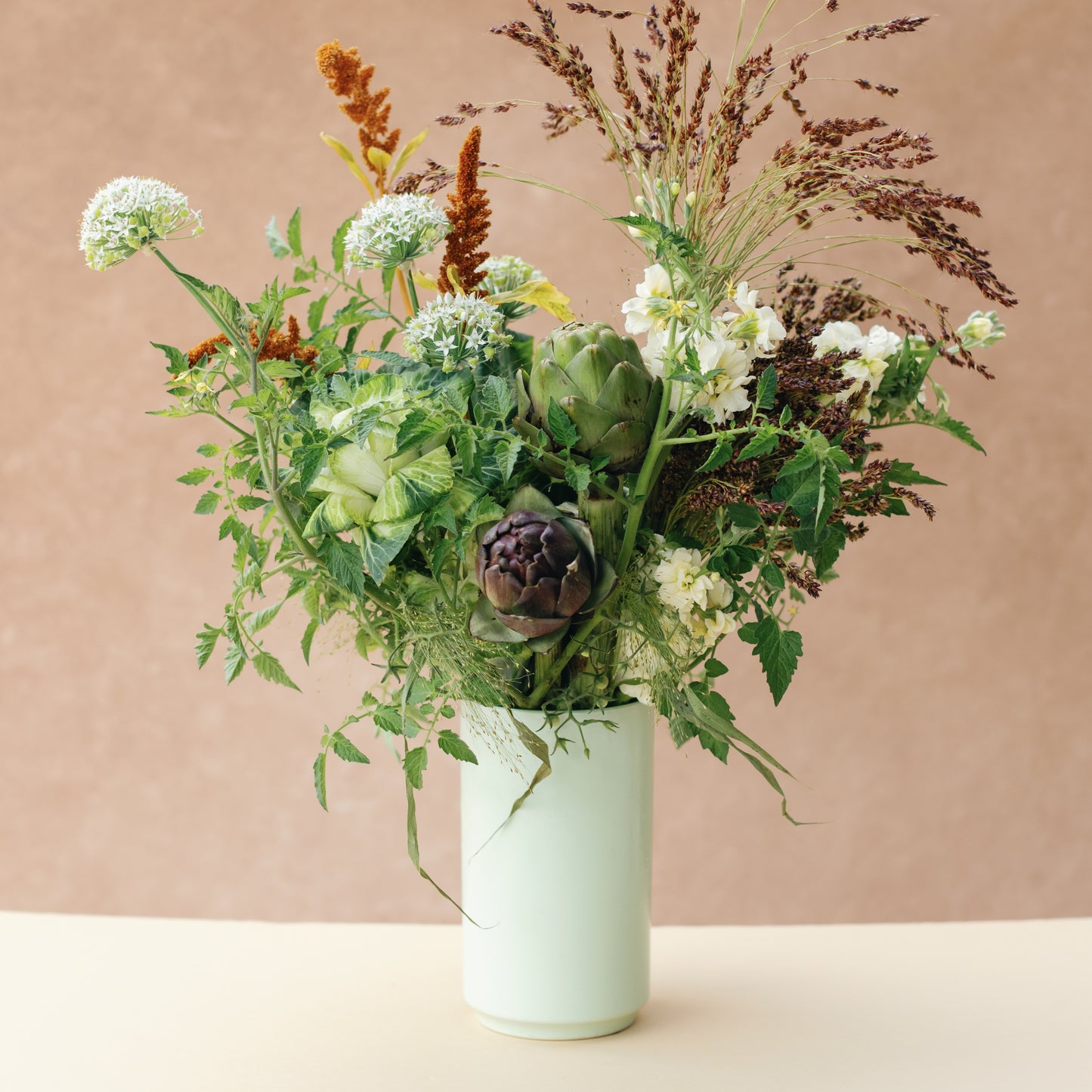 Bouquet of flowers in a light green vase on a beige background