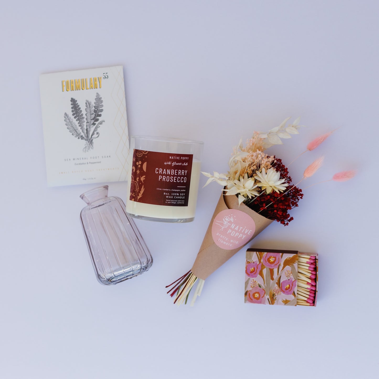 Collection of decorative items including a candle, bottle, matches, and flowers on a white background