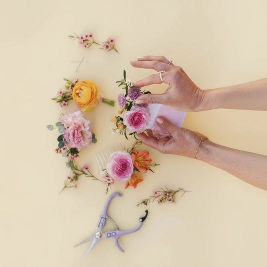 Hands arranging flowers on a yellow background with floral decorations and scissors.