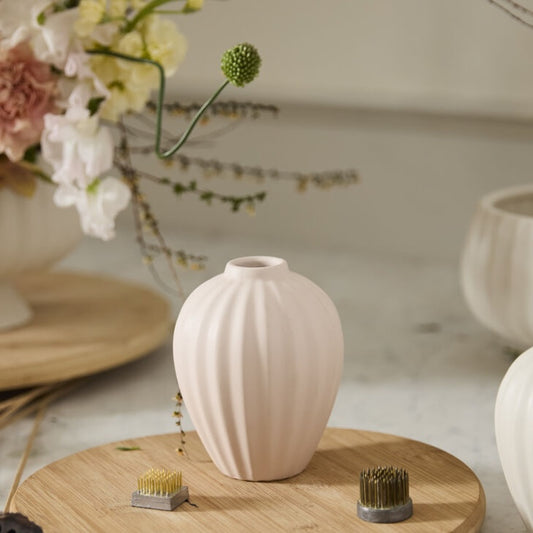 White ribbed vase on a wooden surface with flowers and decorative items in the background