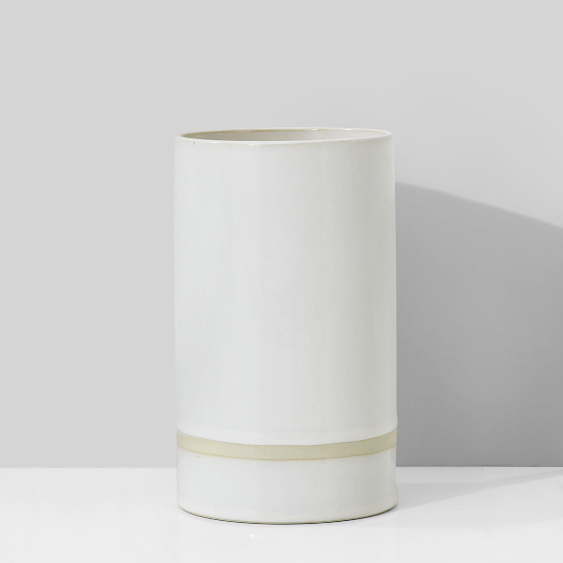 White cylindrical vase with a thin beige band on a light gray background