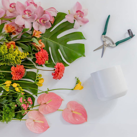 bright tropical flowers and foliage with florist snips and a white vase