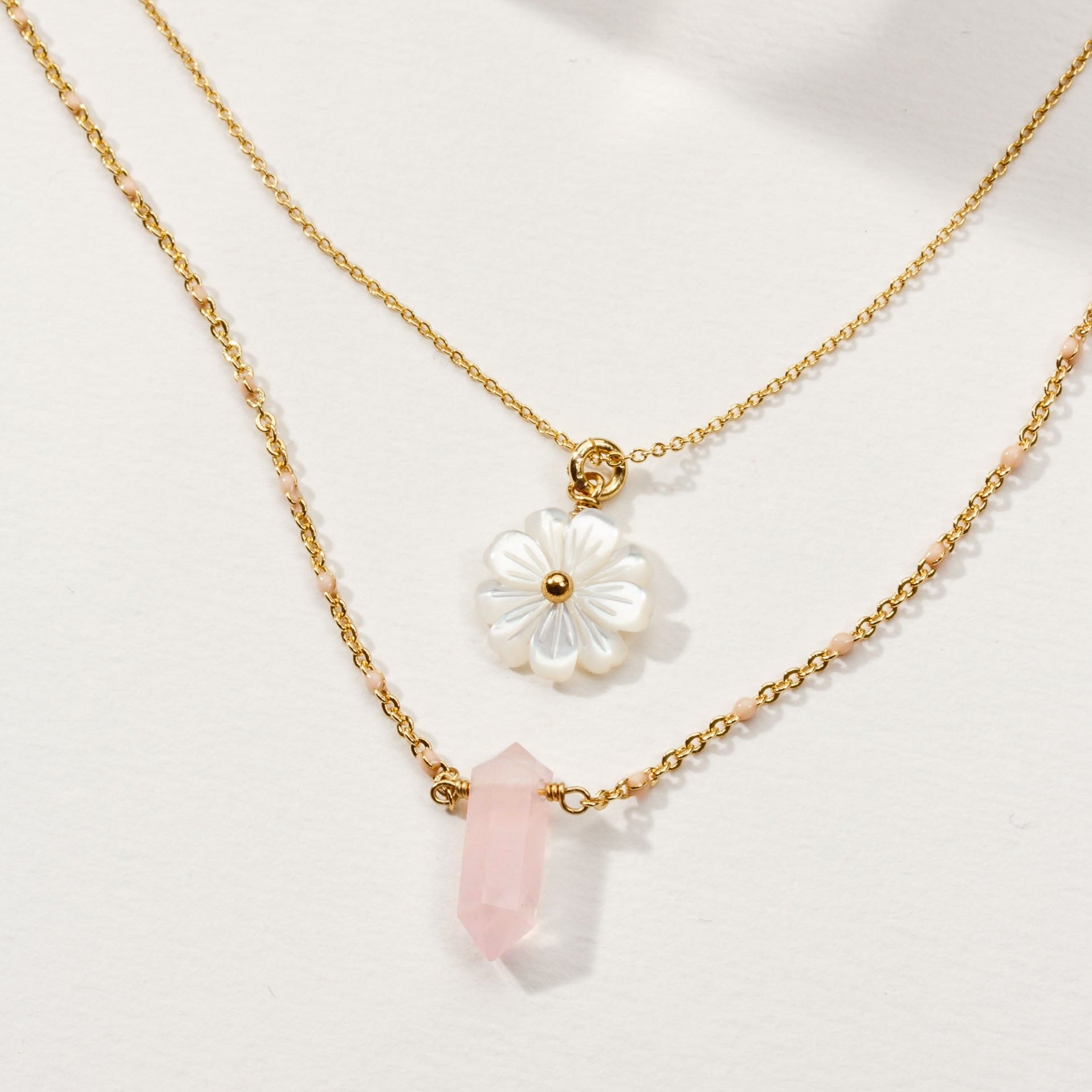Two gold necklaces with floral and crystal pendants on a light background