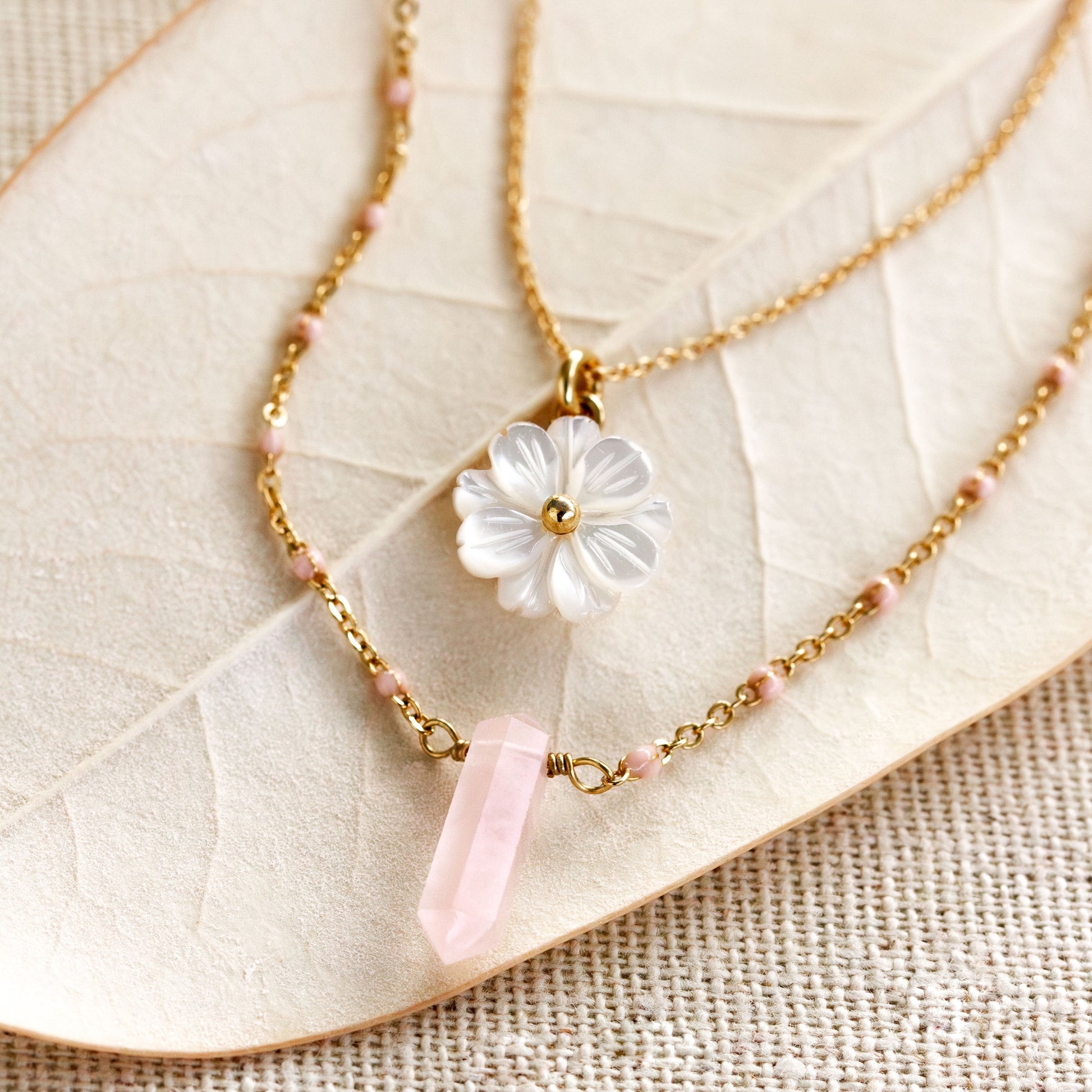 Necklace with a white flower pendant and pink crystal on a beige leaf background