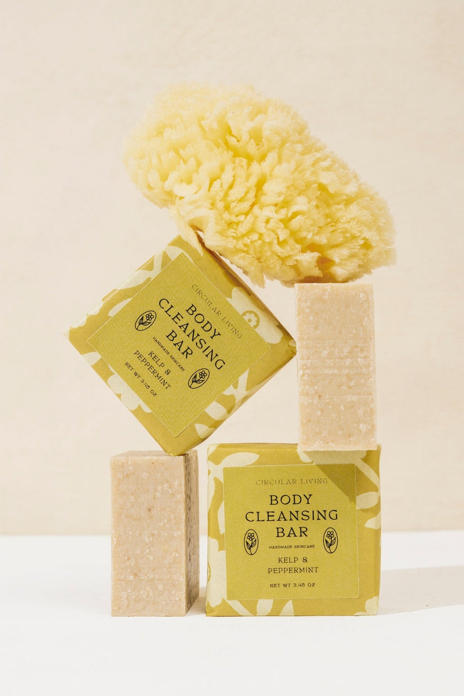 Body cleansing bars with packaging and a yellow sponge on a beige background