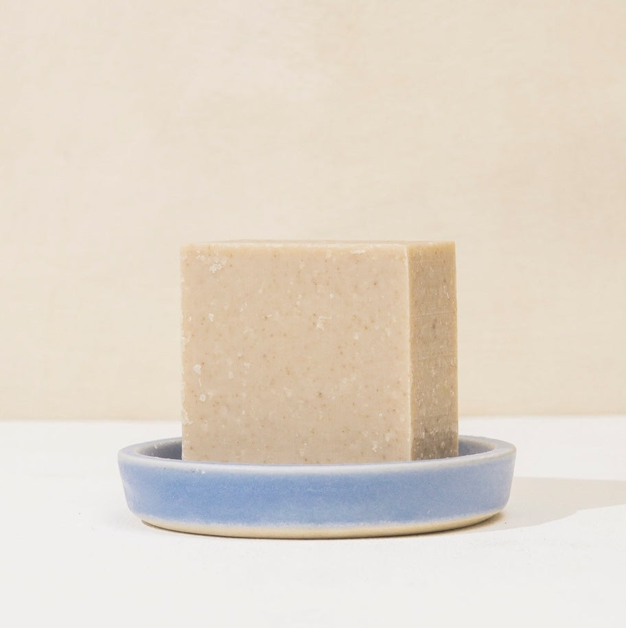 Bar of soap on a small blue ceramic dish against a beige background