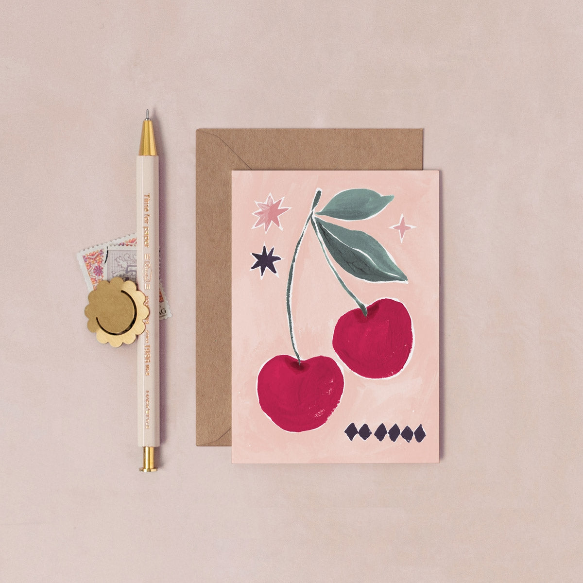 Greeting card with cherry design, pen, and envelope on a beige background