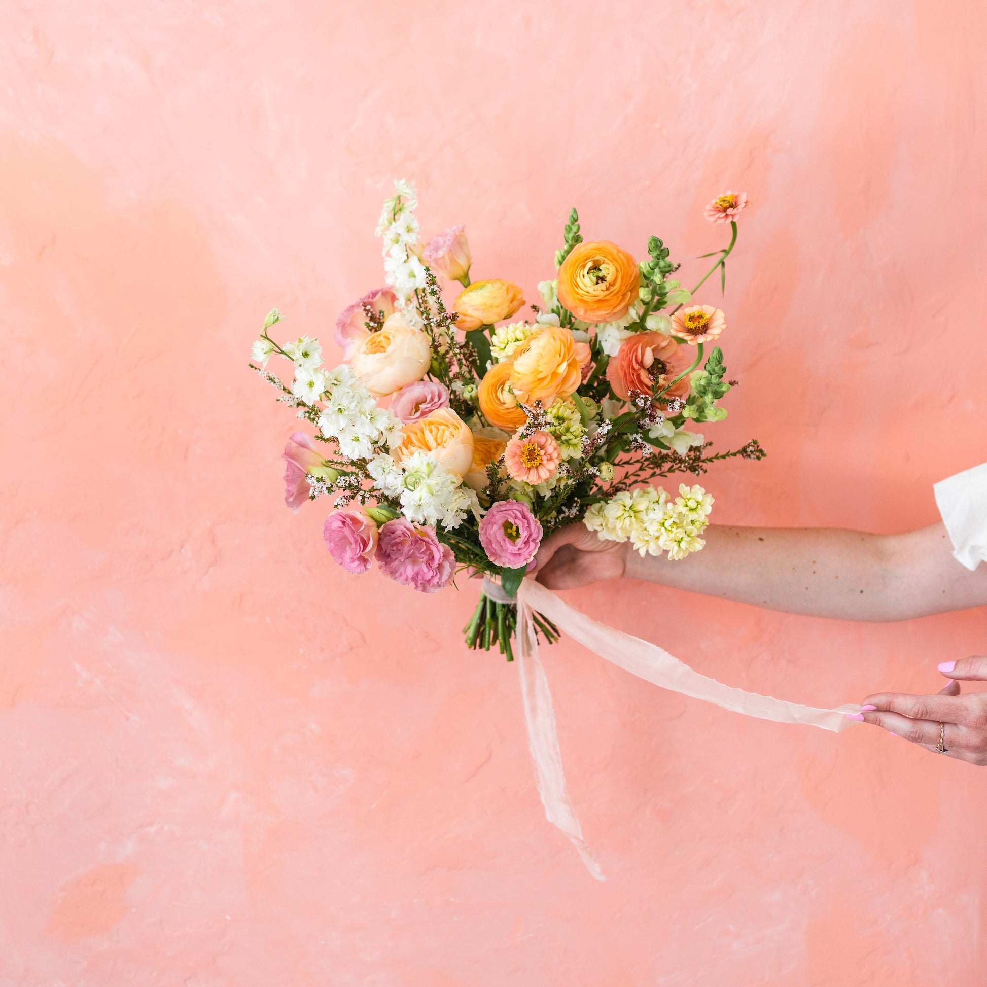 Bouquet of flowers held by a person against a pink background
