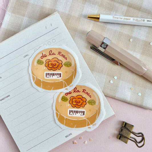 Two round De La Rosa Mazapan stickers on a notebook with stationery items.