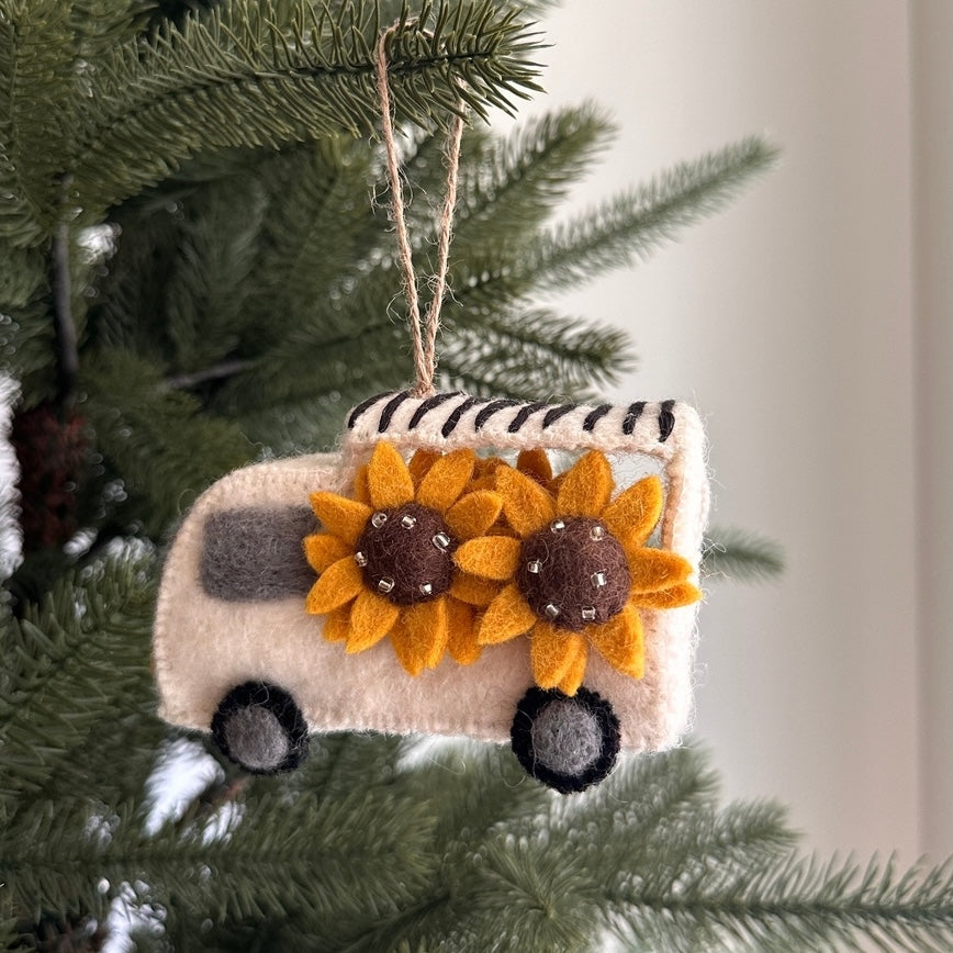 Decorative ornament shaped like a camper with sunflower designs hanging on a Christmas tree.