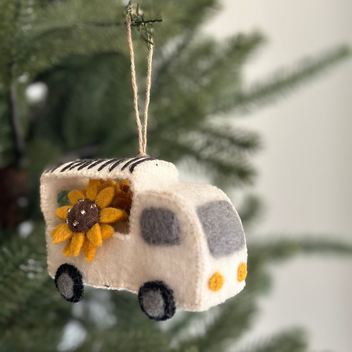 Felt camper ornament with sunflower decoration hanging on a tree.