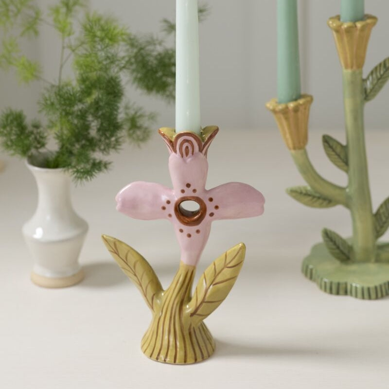 Decorative candle holder with pink floral design on a white surface with plants in the background