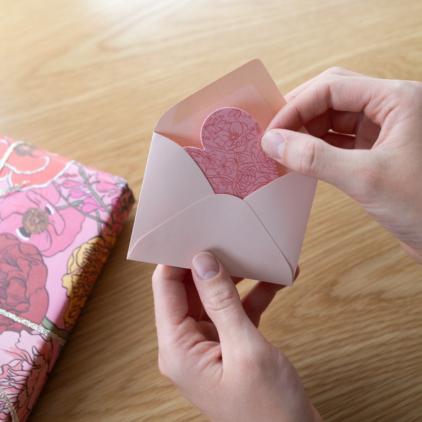 Person holding a pink envelope with floral design on a wooden surface