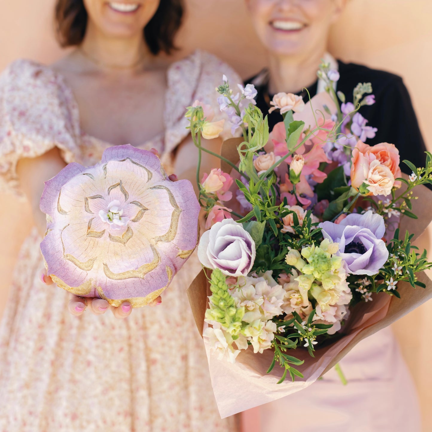 Two people holding a bouquet of flowers and a bread with floral design.