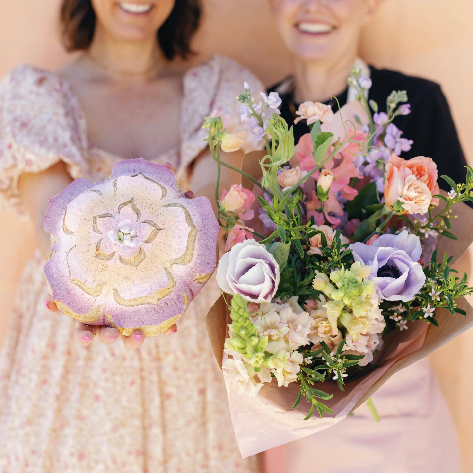 Two people holding a bouquet of flowers and a bread with floral design.