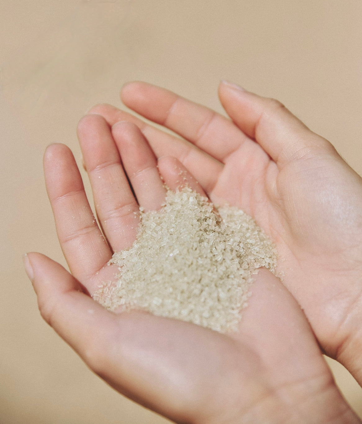 Hand holding a small amount of light green bath salts against a beige background