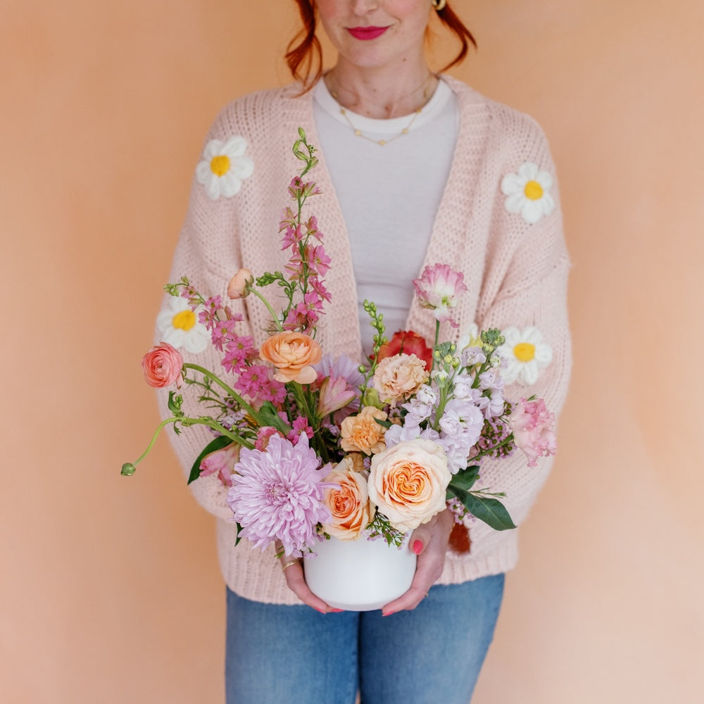 Woman in daisy sweater holds Mother's Day flower arrangement