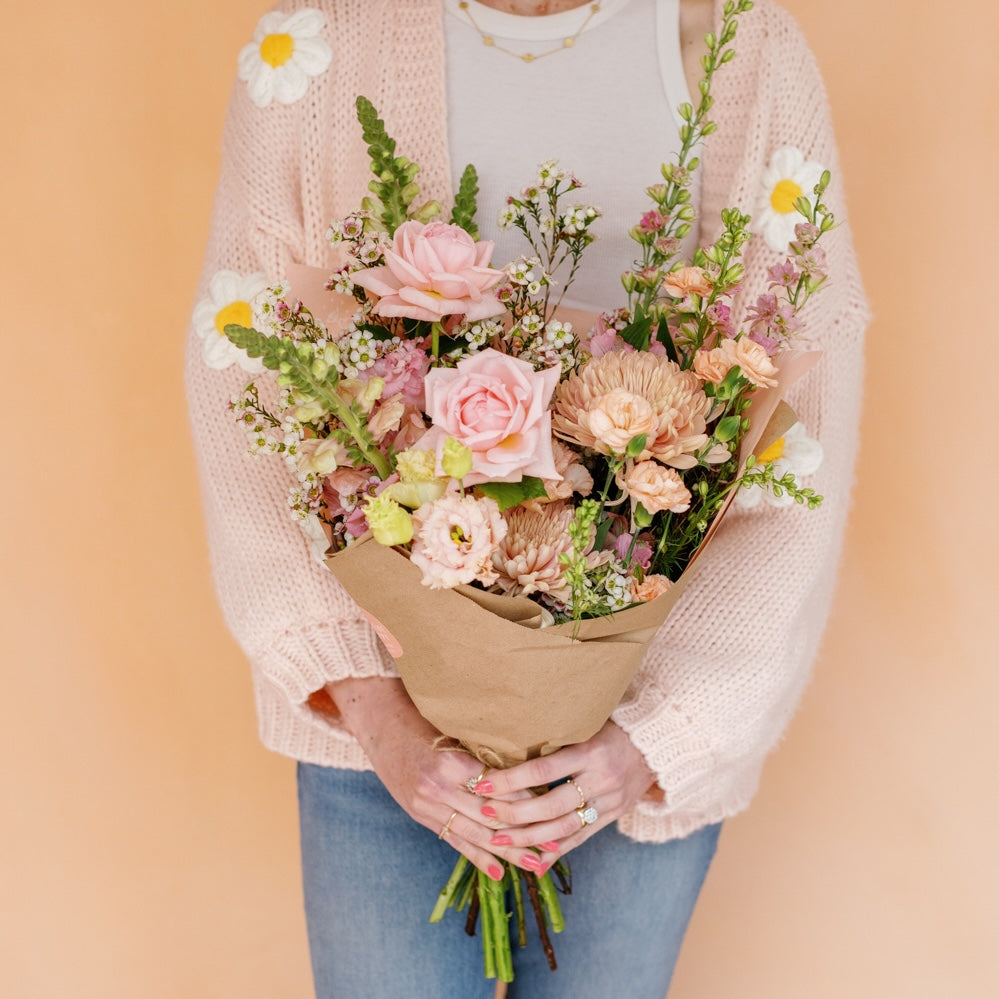 Woman in a sweater holding a flower bouquet from Native Poppy benefitting Susan G Komen
