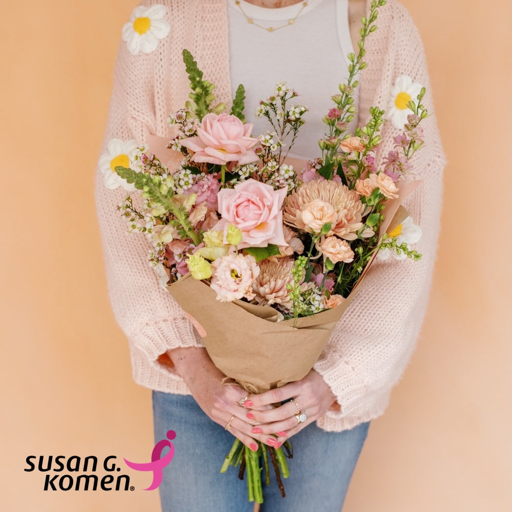 Woman in a sweater holding a flower bouquet from Native Poppy benefitting Susan G Komen
