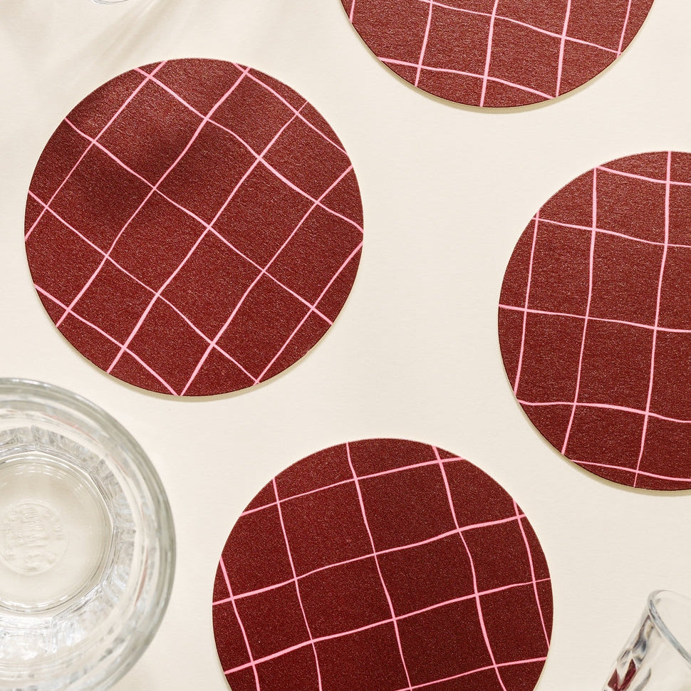 Four round burgundy grid coasters on a light surface with glasses