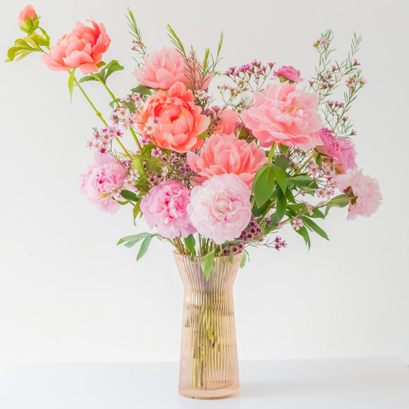 Premium flower arrangement made with multicolored peony flowers in a pink glass jar