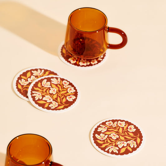 Set of floral coasters with amber glass mugs on a beige background