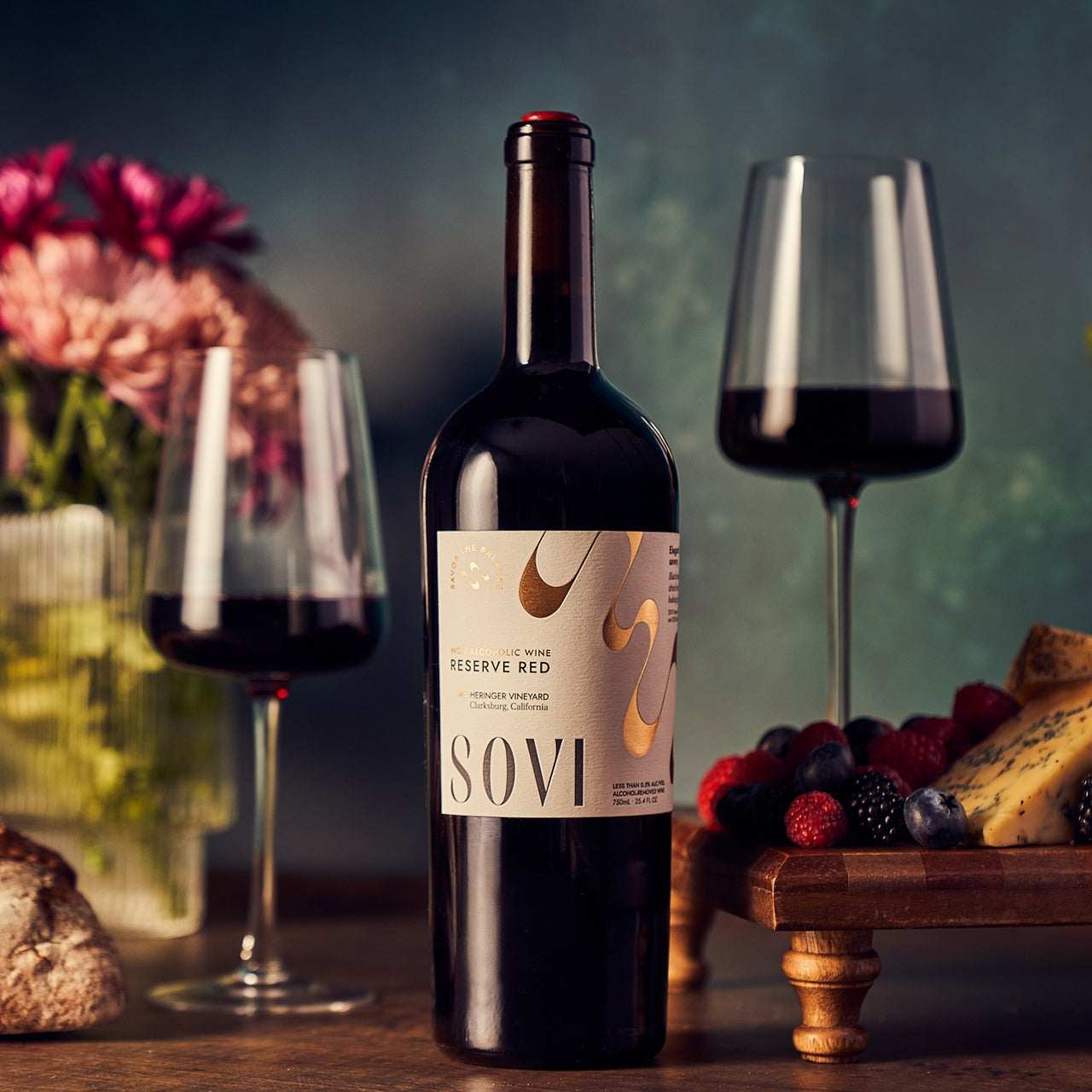Bottle of SOVI Reserve Red wine with two glasses and a plate of snacks on a wooden table.