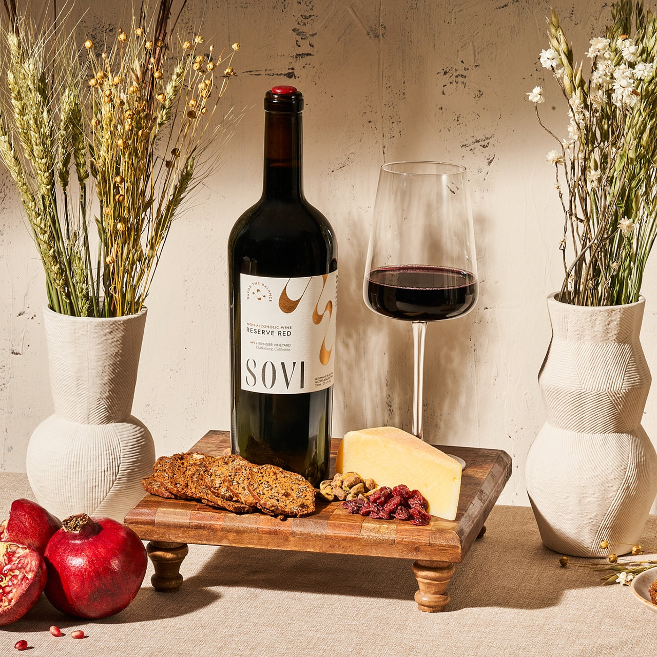 Wine bottle, glass, and snacks on a wooden board with decorative elements.