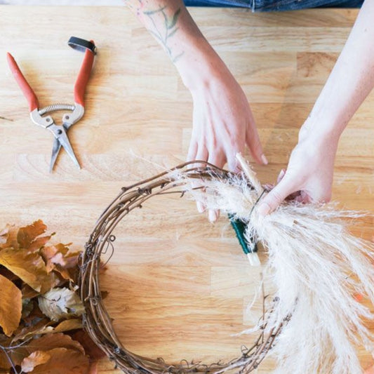 Person crafting a wreath with tools on a wooden surface - Dried Wreath Making Workshop from Native Poppy
