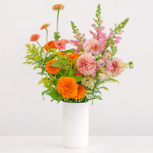 Tall pink and orange flower arrangement in white vase