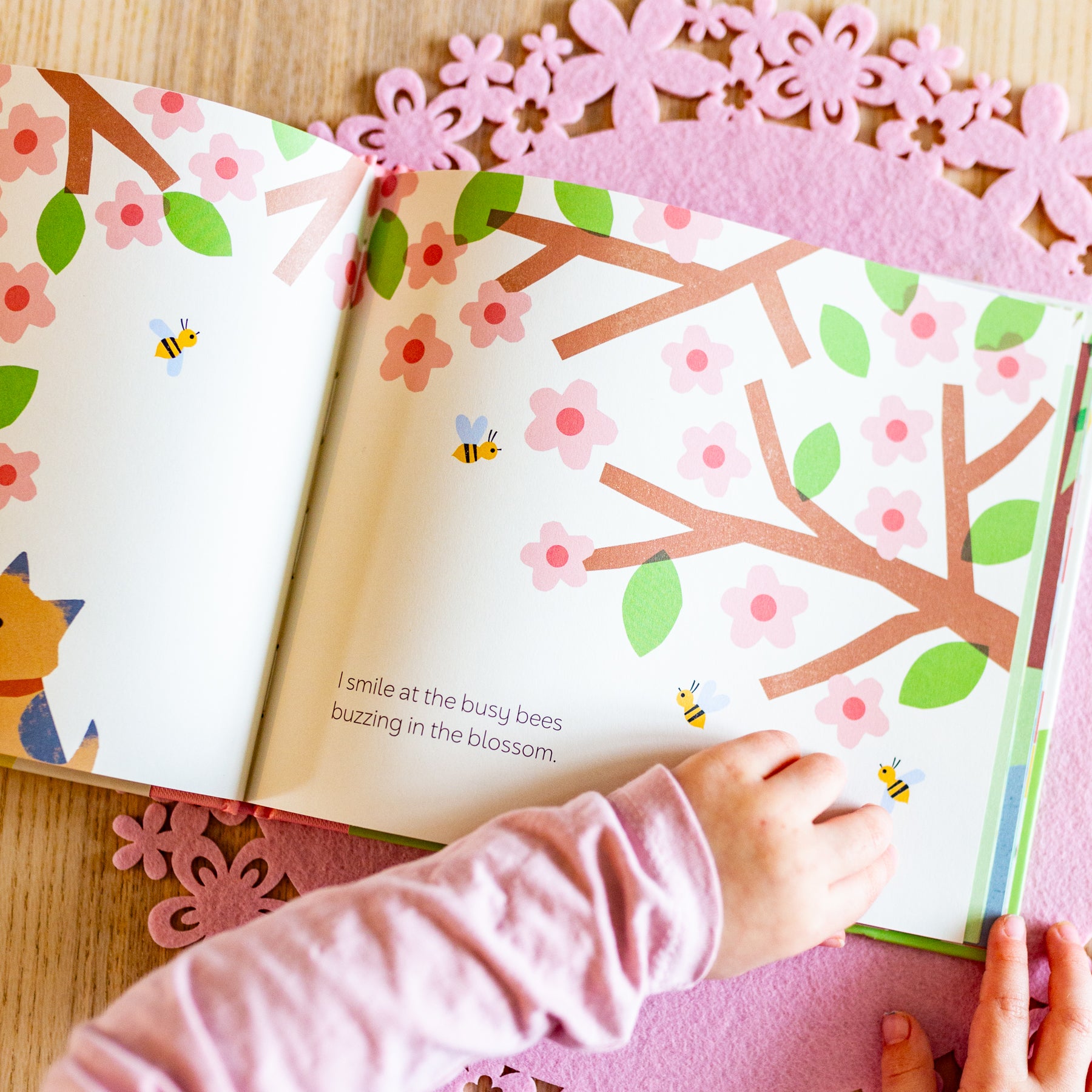 Children's book with floral and bee illustrations on a pink decorative mat.
