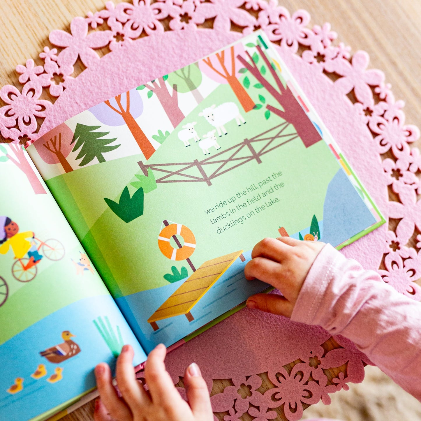 Child's hands holding a colorful children's book with a pink decorative mat underneath.